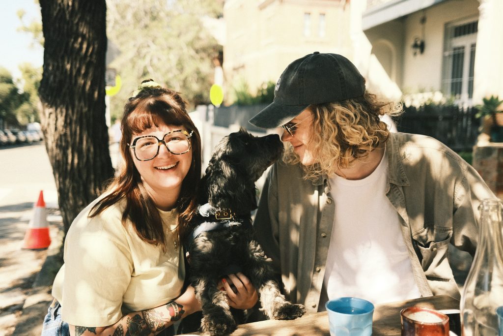couple with black cavoodle at an outdoor table